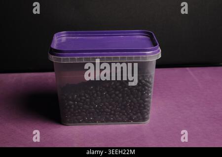 A clear plastic food storage container with a purple lid is filled with dried black beans, ready for cooking or storage Stock Photo