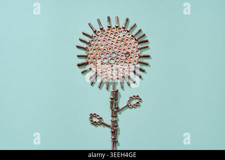 Metal bolts and nuts arranged as abstract flower shape on mint background in minimal style Stock Photo