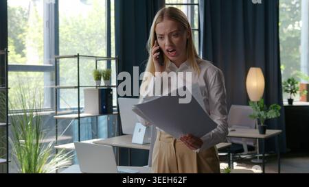 Annoying Caucasian businesswoman talking yelling mobile phone looking in papers hold documents report female girl work conflict quarrel Stock Photo