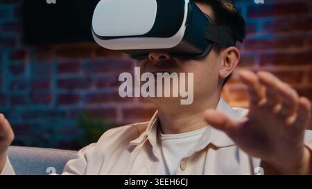 Concentrated Asian adult man using vr interactive interface Korean male in virtual reality glasses enjoying internet simulation online gaming Japanese Stock Photo
