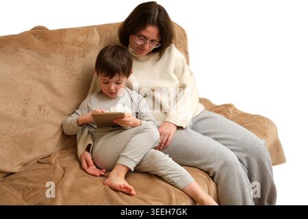 Mother and son sitting on sofa using tablet. Woman and child playing game on digital device at home. Family lifestyle, education, technology, childhoo Stock Photo