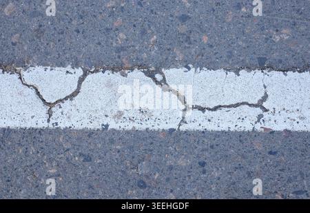 Worn road markings on a road with visible signs of aging and cracks. Detail of urban road markings on asphalt with wear from industrial infrastructure Stock Photo