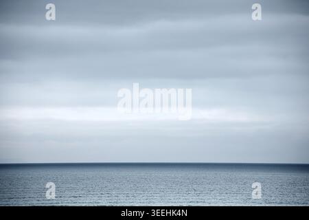 Grey cloudy sky above sea with dark blue horizon Stock Photo