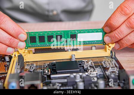 A technician installs a RAM module into a motherboard slot on a wooden workspace. Stock Photo