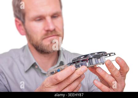 A focused man with a beard holds and inspects a computer graphics card against a white background. Stock Photo