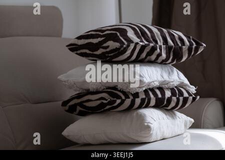 Stack of decorative pillows with zebra pattern and soft neutral cushions arranged on sofa in cozy modern living room interior. Comfortable home stylin Stock Photo