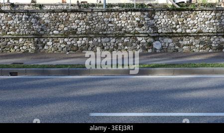 Boundary stone wall with sidewalk and shaded street in front. Background for copy space. Stock Photo