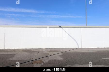 White painted prefab concrete wall with blue cloudy sky on behind and street in front. Background for copy space. Stock Photo