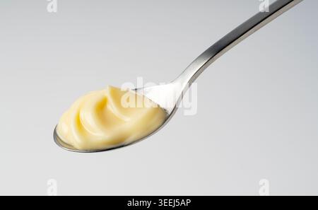 Creamy mayonnaise with elegant swirl on a stainless steel spoon, thick yellow sauce condiment on light gray background Stock Photo