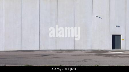 Precast concrete panels wall with metal door and security camera on the right side. Road in front. Background for copy space. Stock Photo