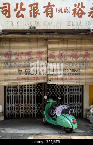 Street scene showing a green moped scooter parked outside a closed roller metal shutter door of a historic shop, George Town, Penang, Malaysia Stock Photo