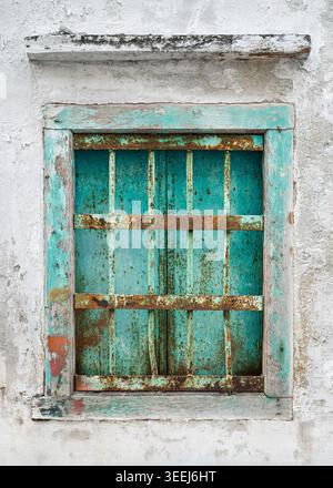 A weathered green window set into a whitewashed wall in the backstreets of Georgetown, Penang, Malaysia. The frame is worn and peeling. Stock Photo