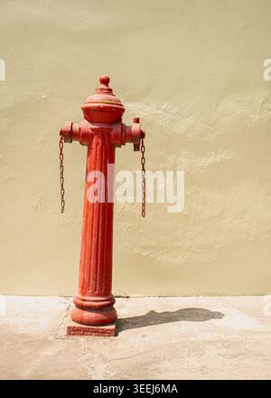 Minimalist front view of a vibrant red metal fire hydrant standing against a plain cream wall background, George Town, Penang, Malaysia Stock Photo