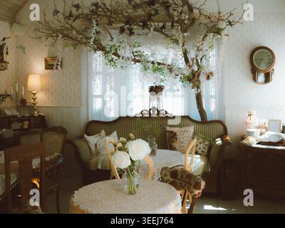 Vintage interior of Ott and Matilda Cafe with lace tablecloth, white peonies, and decorative tree branches in Estonia Stock Photo