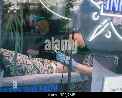 Tattoo artist inking a client's leg seen through a shop window in Tallinn, Estonia, spring Stock Photo