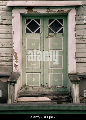 Weathered green wooden door with floral motifs on a peeling white clapboard house in Rakvere, Estonia Stock Photo