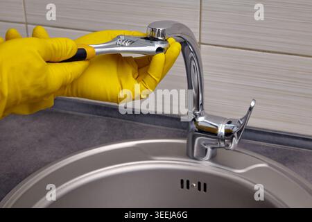 repairing a kitchen sink faucet with gloves and a wrench Stock Photo