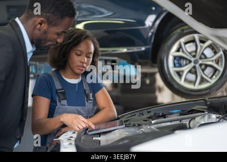 Woman mechanic explaining car problem to client, showing digital diagnostics on tablet. Inclusivity and professionalism in the auto industry. Stock Photo