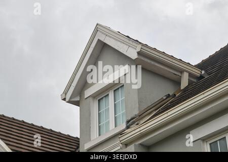 light grey stucco house wall with white window and brown tiled roof, close-up of home construction and property maintenance Stock Photo