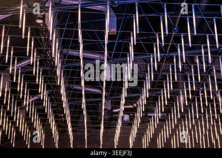 Hanging LED tubes suspended from an industrial metal ceiling grid create a rhythmic, futuristic pattern of warm and cool light, adding texture and amb Stock Photo