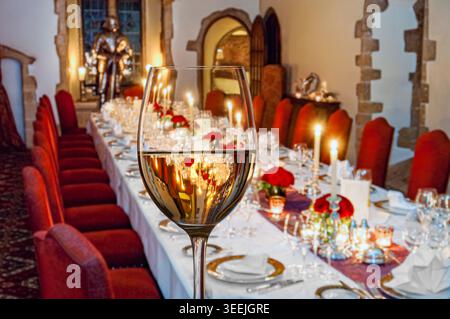 WINE DINNER PARTY TABLE CANDLES FORMAL LUXURY Fine white wine glass with formal seated banquet candlelit dinner party table with suit of armour behind Stock Photo