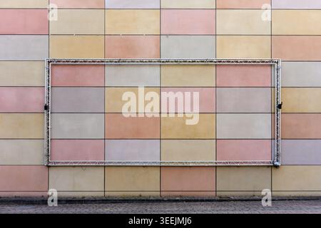 Empty metal billboard frame on a colorful geometric tiled wall. Stock Photo
