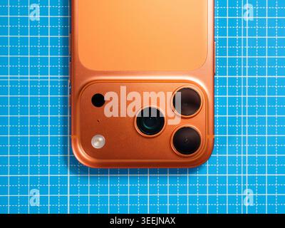 POZNAN, POLAND - MAY 11, 2026: Close-up of the triple-lens camera module and sensors of an orange iPhone smartphone on a blue grid cutting mat. Stock Photo
