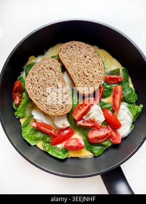Healthy open faced omelette with spinach, cherry tomatoes, mozzarella and two whole grain toast in a pan. Concept for healthy eating, brunch. Stock Photo