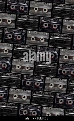 Pattern of vintage transparent and black audio cassettes arranged on a dark background. Stock Photo