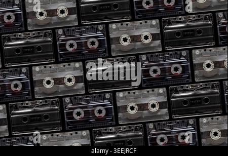 Pattern of vintage transparent and black audio cassettes arranged on a dark background. Stock Photo