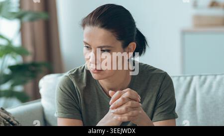 Woman Sitting on Sofa Looking Thoughtful in a Modern Home During the Day Stock Photo