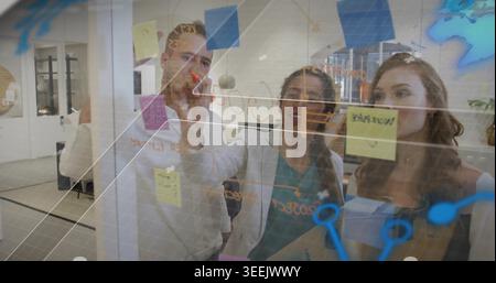 Writing woman using red marker sketching on glass board at office, with sticky notes, in blazers Stock Photo
