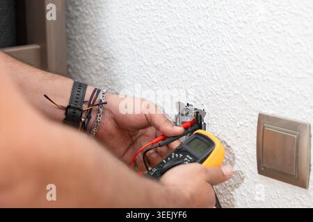 Electrician's hands using a multimeter to check voltage on an electrical outlet Stock Photo
