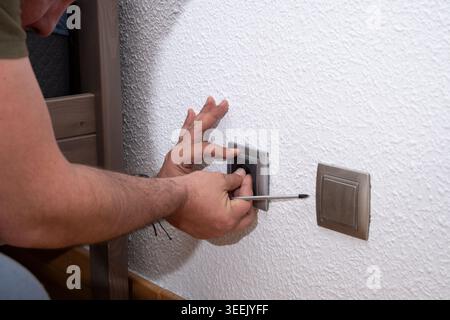 Man installing new electrical wall outlet using a screwdriver during home improvement Stock Photo