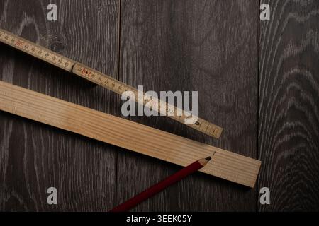 Woodworking flat lay with wooden plank, folding ruler and red pencil on dark wooden background, concept of carpentry, measuring, planning and DIY cons Stock Photo