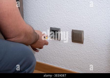 Man installing a new electrical socket on a white wall during home renovation Stock Photo
