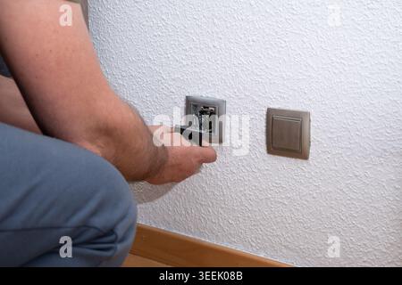 Professional electrician installing new wall outlet and replacing old light switch on wall Stock Photo