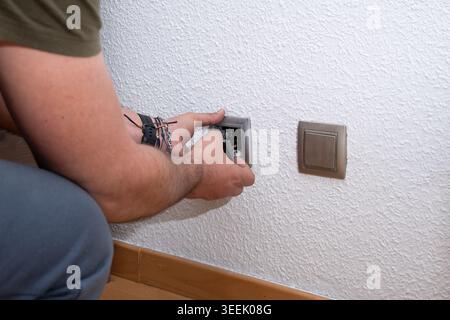Man installing electrical light switch on white wall Stock Photo