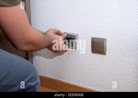 Person's hand installing or repairing an electrical socket on a white wall Stock Photo