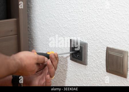 Person fixing electrical wall socket on white wall using a screwdriver Stock Photo