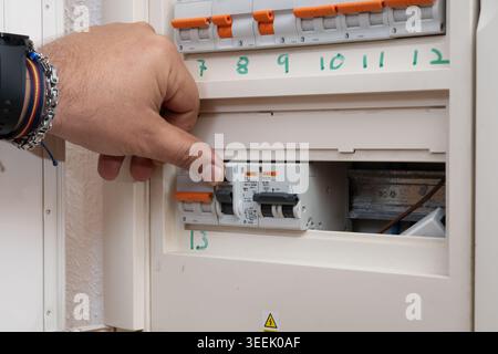 Hand turning on an electrical circuit breaker in a home fuse box, managing power Stock Photo