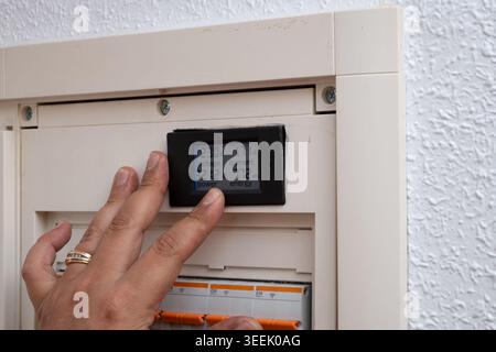 Hand checking electricity consumption on a digital power monitor display in a circuit breaker box Stock Photo