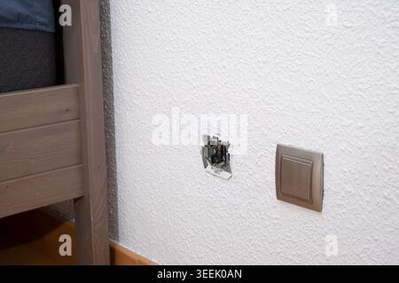 Exposed wiring from a damaged electrical outlet next to a light switch Stock Photo