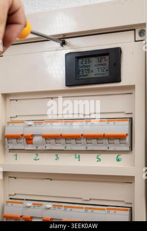 Hand installing smart meter displaying voltage, current, power, and energy in electrical panel Stock Photo