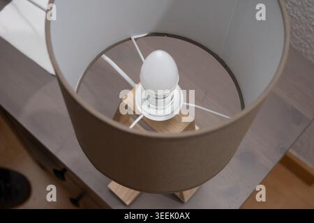 Modern table lamp featuring a brown fabric shade and light bulb on wooden furniture Stock Photo