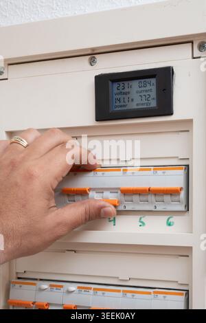 Hand activating a circuit breaker in a home electric fuse box with a digital meter revealing power consumption Stock Photo