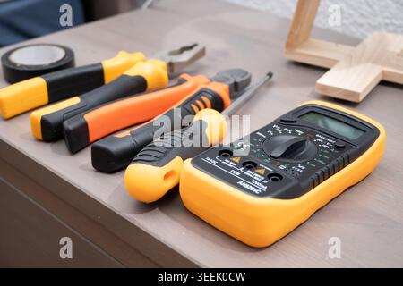 Multimeter and various electrical tools resting on a wooden surface, ready for repair work Stock Photo