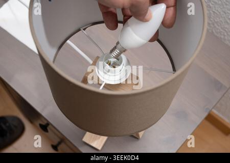 Hand changing a new energy-efficient LED light bulb in a desk lamp Stock Photo