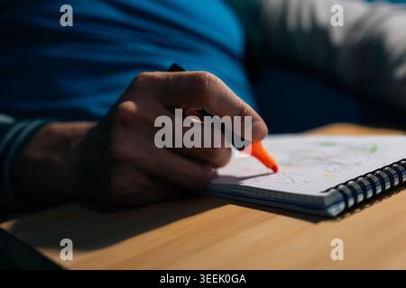 Person hand holding an orange highlighter marker, sketching and actively drawing ideas on spiral bound notebook page, focusing on creativity and plann Stock Photo