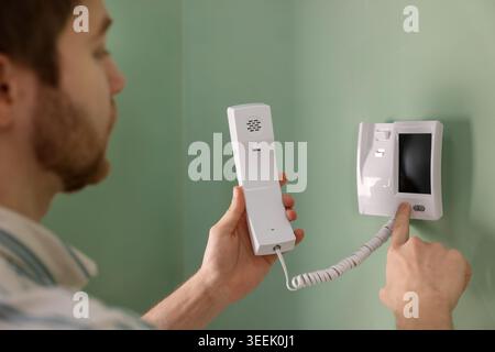 Man with handset pressing button on intercom panel indoors, closeup Stock Photo